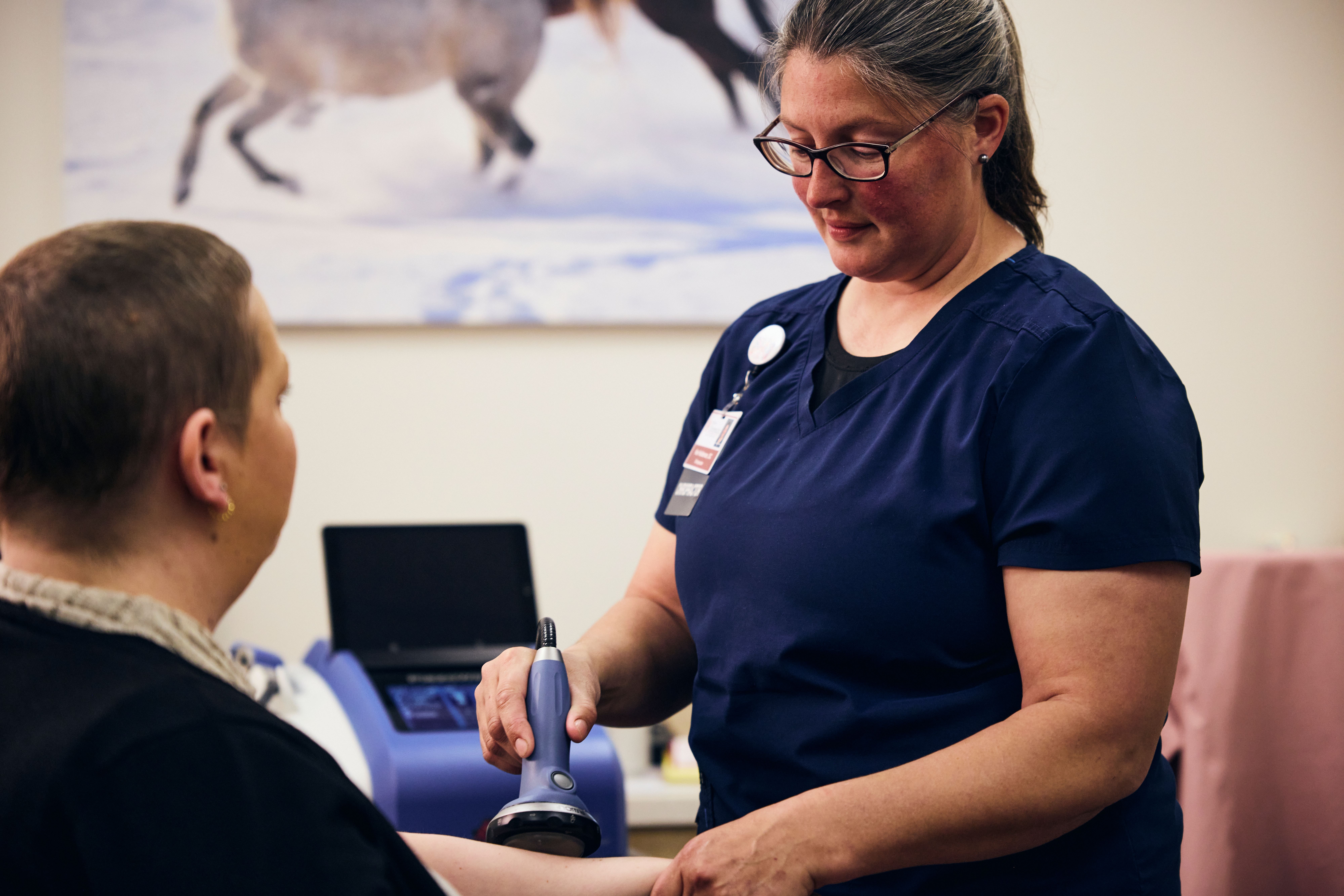 A chiropractor places a laser device on a patient's forearm.