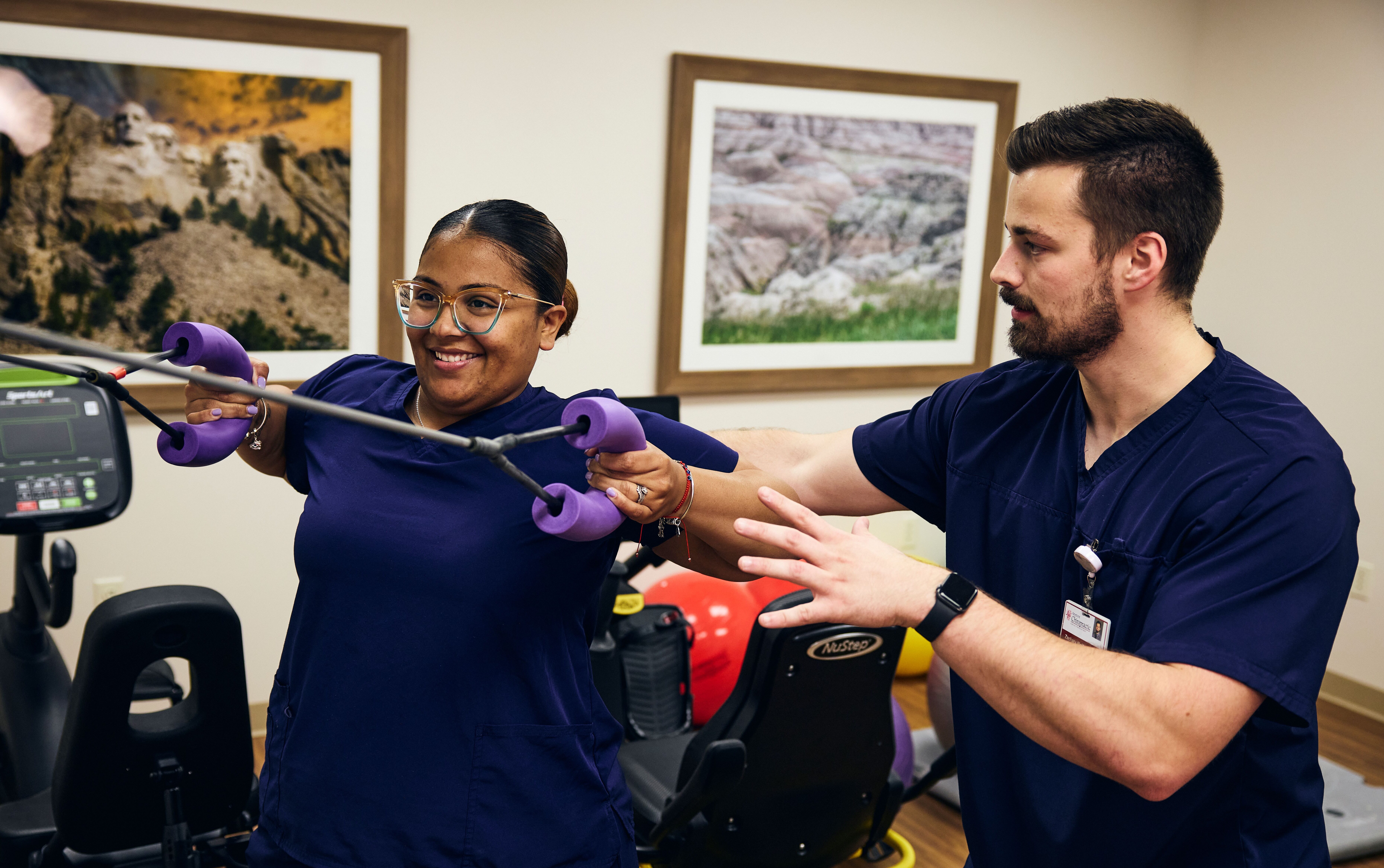 A chiropractor assists a patient with using a weight exercise machine